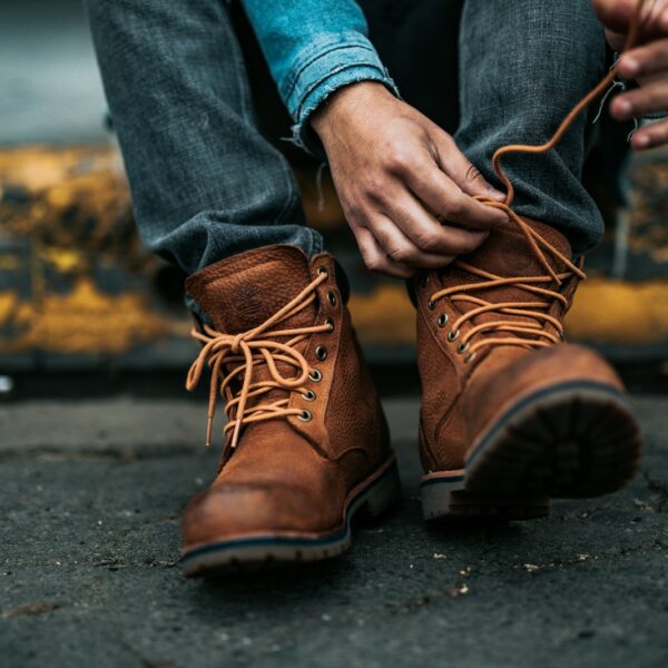 person sitting on yellow gutter tying up his left boot's laces